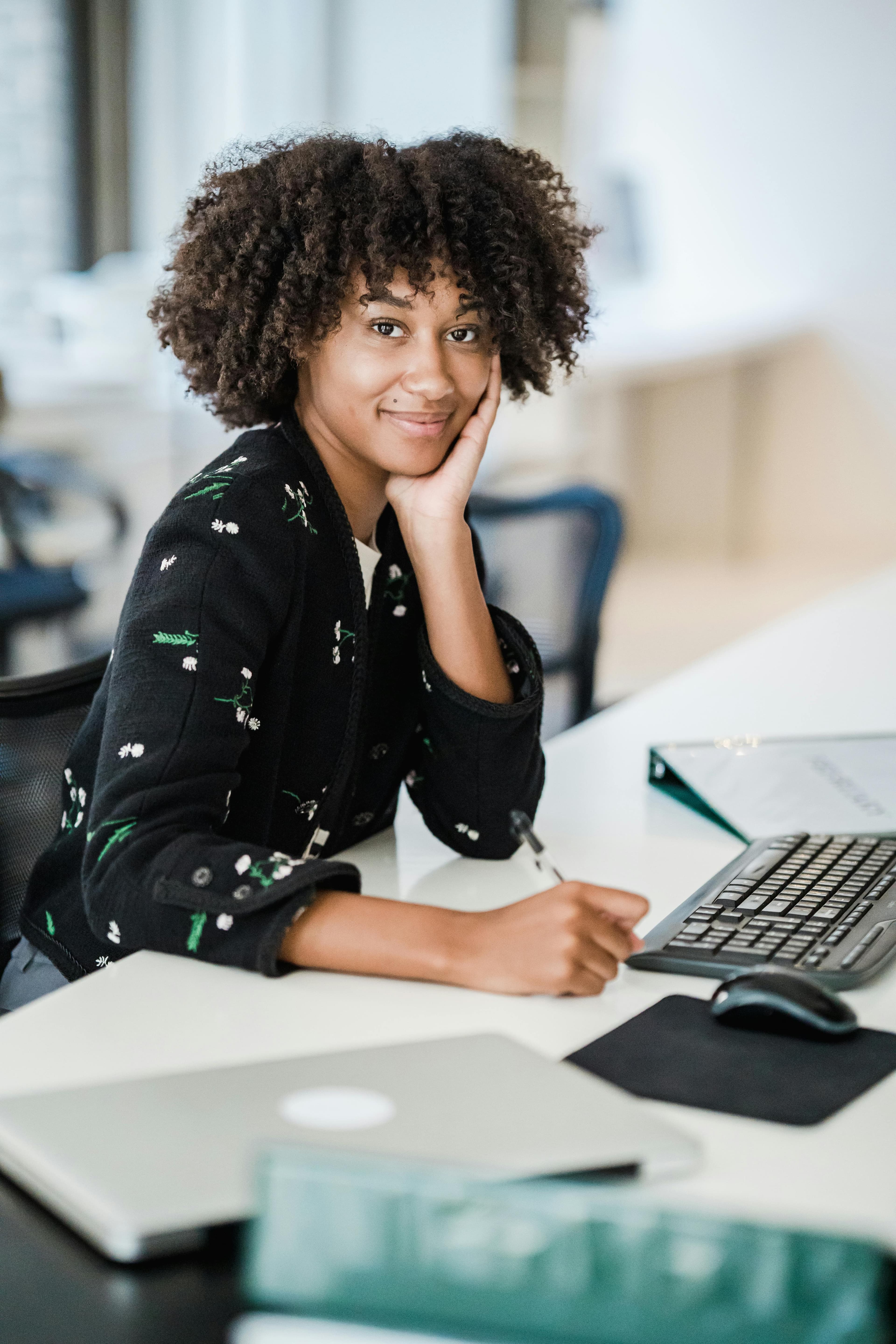 A woman sitting on a desk in front of the computer working.